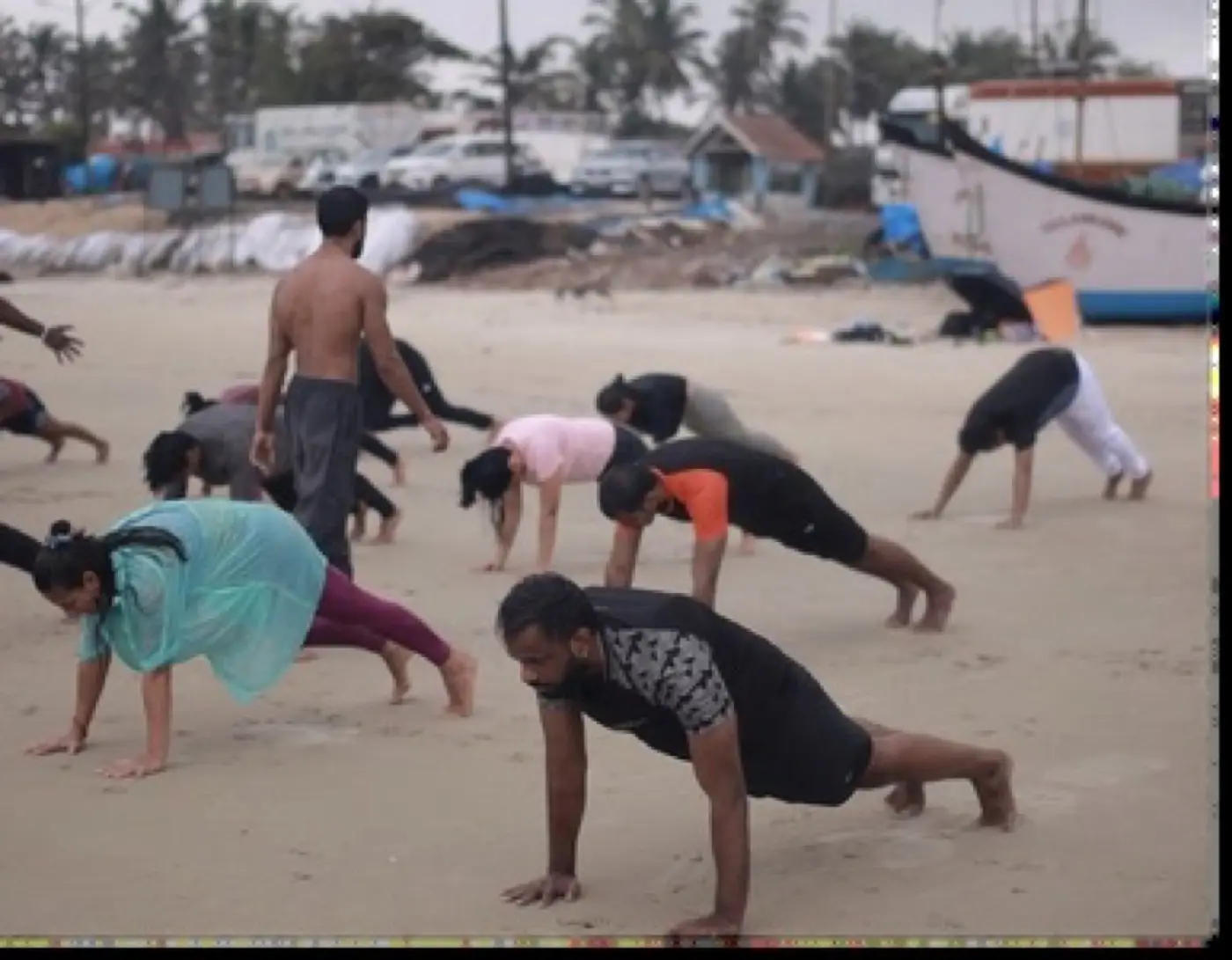 Group of beginners and athletes doing push-ups together on the beach